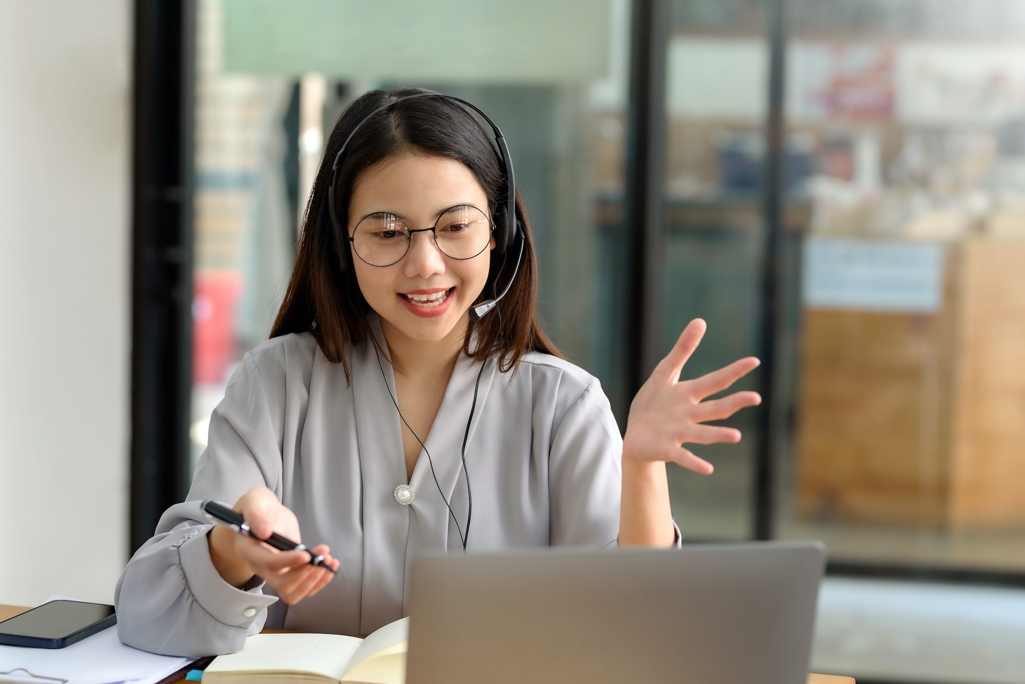 Happy young Asian student woman wearing headphones looking at webcam, looking at camera