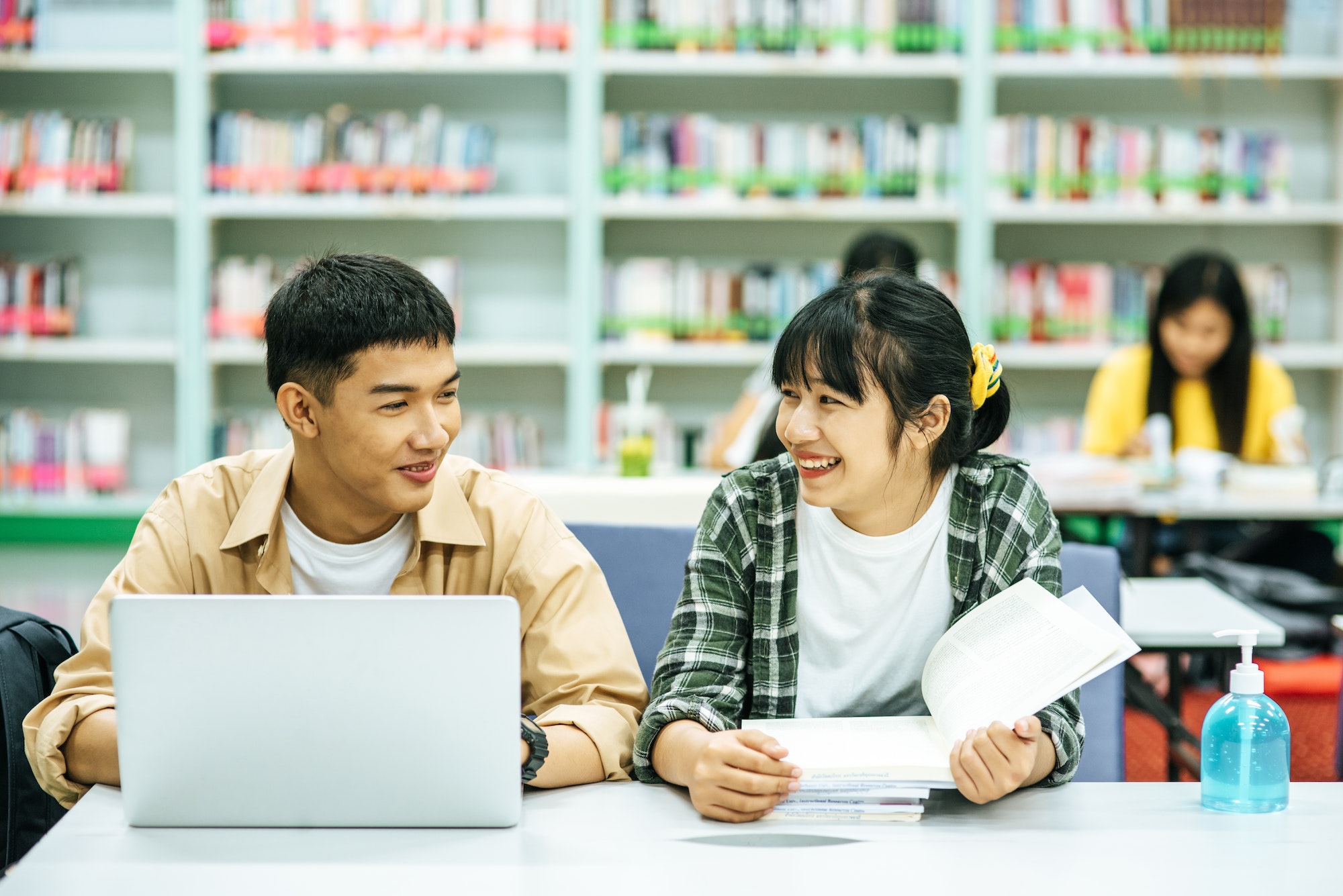 Women read books and men use laptops to search for books in libraries.